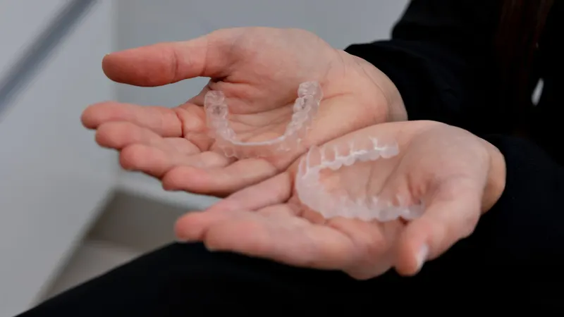 Duas mãos em concha seguram dois alinhadores ortodônticos transparentes, vistos de perto contra uma parede clara