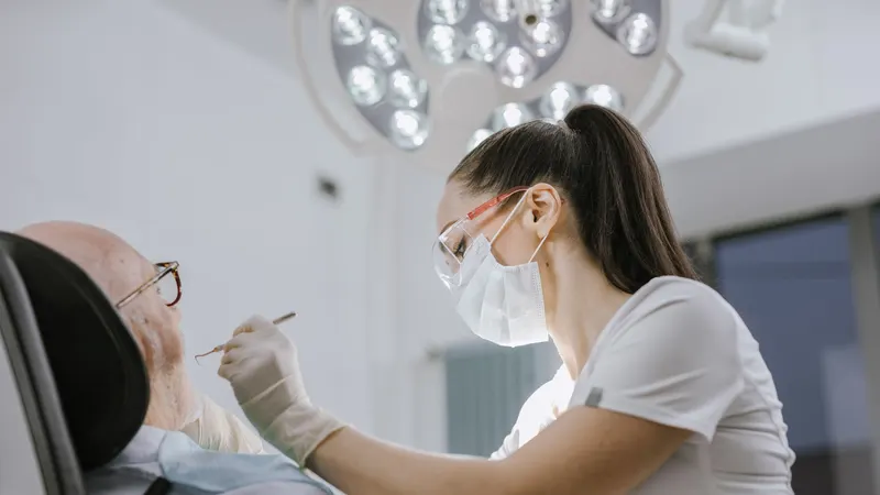 Dentista de máscara e óculos de proteção examina um paciente na cadeira odontológica