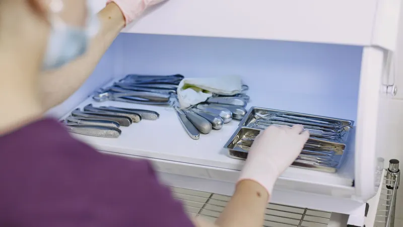 Profissional de luvas e máscara organizando instrumental odontológico esterilizado numa gaveta aberta de armário branco